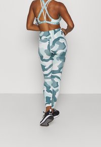 Leggings sportivi in camouflage blu chiaro e un reggiseno sportivo abbinato con fasce incrociate, realizzati in tessuto elasticizzato. Le scarpe da ginnastica nere completano il look.
