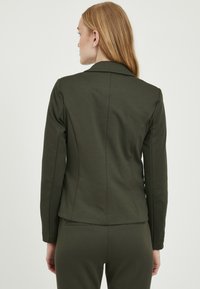 Dark green fitted blazer with a smooth texture, long sleeves, and notched collar. Features back seams and a clean silhouette.