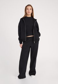 Sudadera negra con cremallera en el frente, corte oversized y dos bolsillos; combinada con pantalones de chándal negros de corte holgado, hechos de una tela suave.