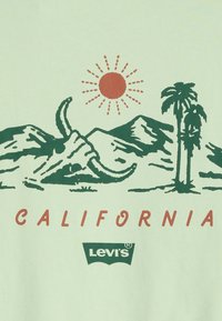 Svijetlozeleni majica s grafikom planina, lubanje bika, palmi i sunca te natpisom "CALIFORNIA" u crvenoj boji. Uključeni logo Levi's.