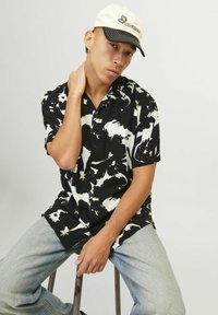 Kortærmet skjorte i sort og hvid med abstrakt blomsterdesign, der har knap-op-lukning. Lette lyseblå denimjeans. Lys kasket.