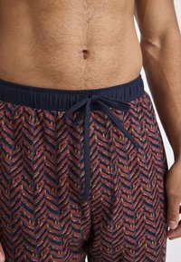 Geometrisch bedrukte pyjamashorts met een rood en marineblauw zigzagpatroon en witte en gouden accenten. Elastische tailleband met verstelbare koordjes.