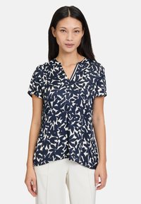 Blusa corta a maniche corte blu navy e crema con motivo a foglia, scollatura a V, taglio dritto e una texture di tessuto leggera e liscia.