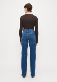 Visoko pasovane modre kavbojke z ožjim krojem in rahlo razširjenim hlačnicama. Imajo dve zadnji žep in klasičen dizajn s petimi žepi.