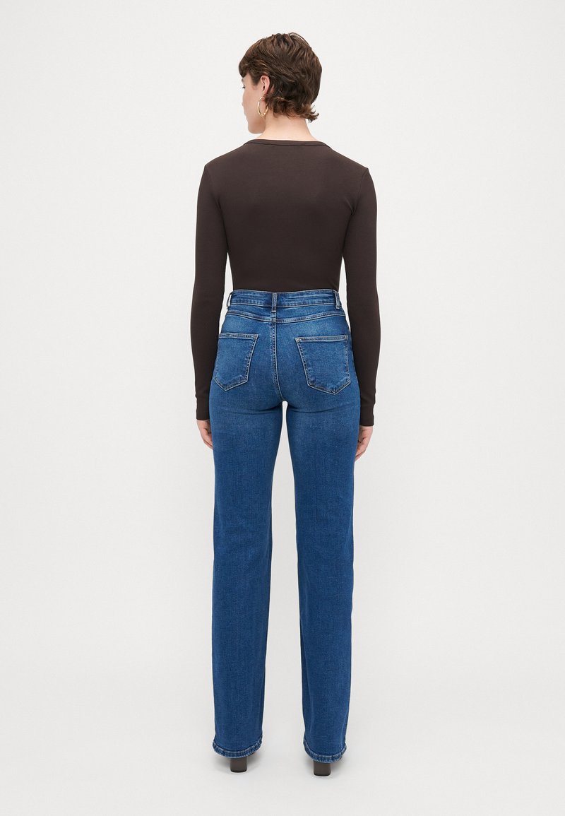 Jeans in denim blu a vita alta, con una vestibilità slim e gamba leggermente svasata. Presentano due tasche posteriori e un classico design a cinque tasche.