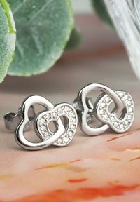 Silverfärgade hjärtformade örhängen med sammanflätad design, prydda med klara rhinestones längs den yttre kanten. Blank metallisk yta.