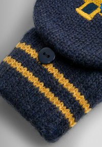 Villavaate tummasinises, kollaste triipudega, ümmarguse klapiga ja tumeda nööbikinnitusega; nähtav tekstuuritud kudumismuster.