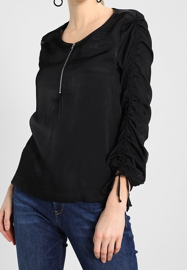 Blusa nera con scollo tondo, zip frontale e maniche gatherate. Tessuto morbido con una leggera lucentezza e lacci regolabili alle estremità delle maniche.
