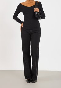 Schwarzes geripptes Langarmoberteil mit schulterfreiem Design, kombiniert mit schwarzen weit geschnittenen Jeans. Accessoires sind eine kleine schwarze Handtasche und besetzte Absatzschuhe.