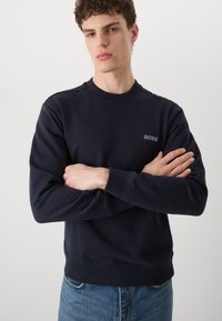 Sudadera azul marino de algodón, con cuello redondo y puños acanalados, y un pequeño logo bordado de "BOSS" en el pecho.