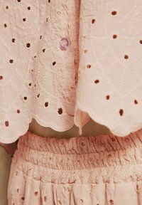 Pink cotton outfit featuring an embroidered top with eyelet details and scalloped hem, paired with a matching smocked waistband skirt.
