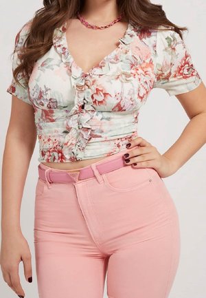 Woman wearing a ruffled floral crop top with short sleeves and high-waisted pink pants with a matching pink belt.