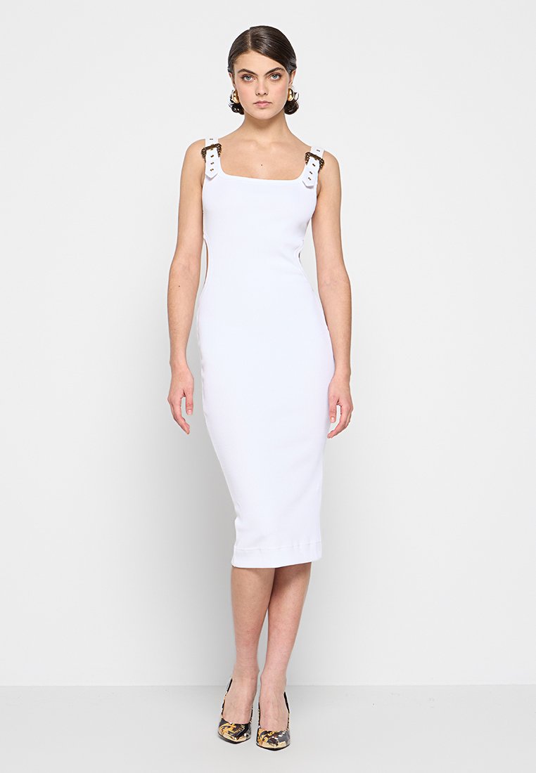 Vestido blanco ajustado con escote cuadrado, lados con cortes y tirantes decorativos. La modelo lleva tacones estampados. Tela suave y elástica.