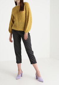 Sinapinkeltainen, teksturoidusta neuloksesta valmistettu pusero, jossa on pallohihat. Yhdistetty mustavalkoraidallisiin lyhytlahkeisiin housuihin ja vaaleanpunaiseen korolliseen mules-kenkään.