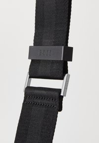 Fekete szőtt nylon pánt sima textúrával, matt fekete műanyag csattal, amelyen a "BOSS" felirat található, és ezüst színű fém kiegészítők.