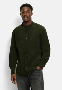 Dunkelgrünes Langarmhemd mit Stehkragen, Knopfverschluss und einer Brusttasche. Der Stoff wirkt strukturiert und lässig.