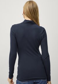 Marineblå langærmet top med cowl-neck design, tætsiddende form og glat tekstur. Bæres med blå jeans, som viser bagved.