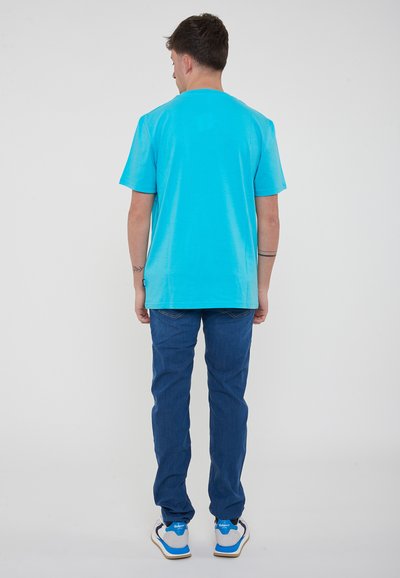 T-shirt turchese a maniche corte con scollatura rotonda, abbinata a jeans blu scuro a gamba dritta e sneakers bianche con dettagli blu.