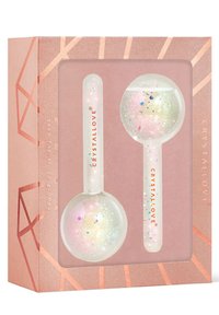 Due cristalli di ghiaccio per il viso in una scatola regalo, con materiale trasparente e glitter iridescenti, su uno sfondo a motivi rosa e oro rosa.