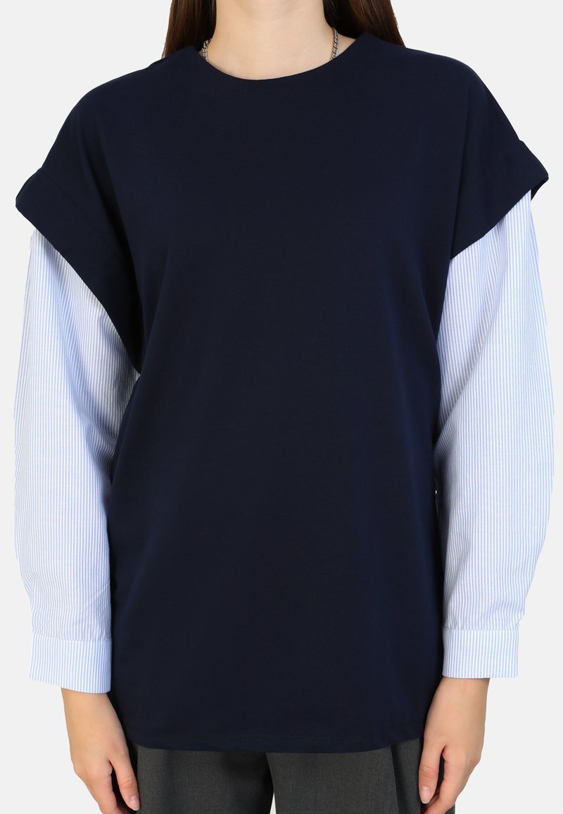 Kragenloses, dunkelblaues T-Shirt mit kurzen Ärmeln; darunter befinden sich lange Ärmel mit weißen Nadelstreifen, die einen Layer-Look und einen Kontrast in den Stoffen erzeugen.