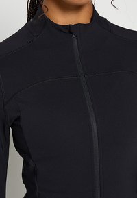 Czarna sportowa kurtka z zamkiem błyskawicznym, wykonana z teksturowanej, prążkowanej tkaniny, z przeszyciami na ramionach i bokach.