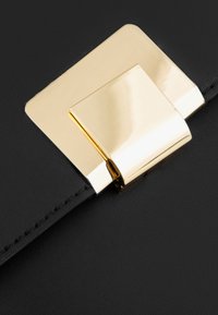 Svart läderclutch med en framträdande fyrkantig lås i guld-ton. Texturen är slät med synliga sömmar längs kanten.