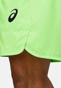 Pantaloni sportivi verde neon con logo nero, caratterizzati da una texture liscia, un orlo curvo e una fessura laterale per migliorare la mobilità.