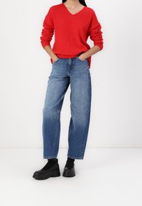 Suéter de punto rojo con escote en V, combinado con jeans de talle alto en azul claro y zapatos de plataforma negra. Diseño sencillo y de ajuste relajado.