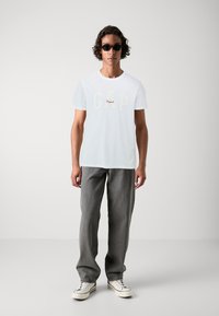 White cotton t-shirt with "GAP" logo in cream and red, paired with loose gray denim pants and white sneakers with blue accents.