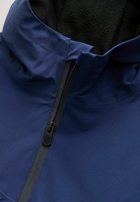 Marineblauw jack met een zachte zwarte fleece voering, hoge kraag en een contrasterende ritssluiting met een gestructureerd trekkoord. Glad buitenmateriaal.