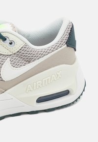 Sneaker in rete grigio chiaro con accenti in suede beige, tallone verde scuro e suola intermedia bianca con logo "AIRMAX" e unità d'aria visibile.