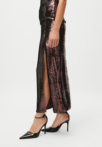 Juodas suknelė su aukštu plyšiu ir metaliniu rožiniu, pasižyminti prigludusia siluetu ir blizgančiais blizgučiais, derinama su juodais stiletai.