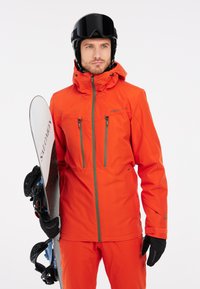 Giacca da neve arancione brillante con cerniere grigie e due tasche sul petto, abbinata a pantaloni coordinati, guanti e una tavola da snowboard. Casco nero e occhiali.
