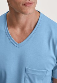  Lichtblauwe katoenen t-shirt met een v-hals, korte mouwen en een klein borstzakje. Gladde textuur, minimale stikseldetails.