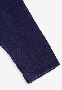 Námorníckom modrý velúrový materiál s ryhovanou textúrou. Na obrázku je vidieť okraj rukáva, ktorý má prehnutý lem pre štruktúru.