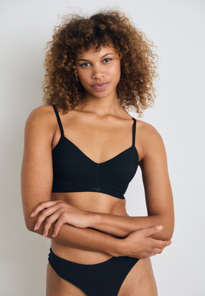 Bralette nera realizzata in tessuto morbido, con un design a V sul collo, spalline sottili e regolabili, e un branding minimalista alla base.
