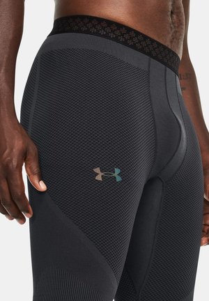 Nahaufnahme einer Person, die schwarze, strukturierte sportliche Kompressionsshorts trägt, mit einem Under Armour-Logo auf dem Oberschenkel und einem sichtbaren Design des Taillenbunds.