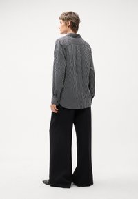 Camicia a righe bianca e nera, con maniche lunghe e colletto classico, abbinata a pantaloni neri a gamba larga. Scarpe basse.