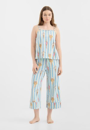 Vrouw draagt een mouwloos blauw-wit gestreept topje en korte broek bedrukt met vintage-zwemmers in verschillende poses.