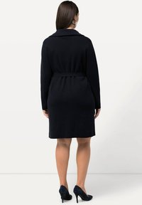 Vestido azul marino con cinturón, mangas largas y cuello con muesca; textura suave y diseño a la altura de la rodilla, acompañado de zapatos de tacón alto en azul marino.