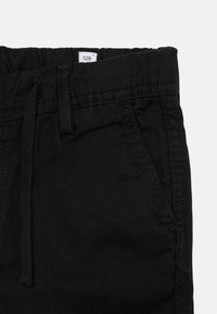 Calções pretos de algodão com uma cintura elástica, cordão ajustável e bolsos laterais, apresentando uma textura suave e uma costura limpa.