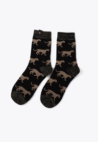 Svarta strumpor med ett upprepande mönster av ljusbruna leopardfläckar. Har en texturerad avslutning och en kontrasterande mönstrad tå.