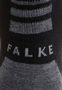 Grau und schwarz gestreifte Socke aus weichem Stoff, mit gerippter Textur und dem Markennamen "FALKE", der in kontrastierenden Buchstaben eingestrickt ist.