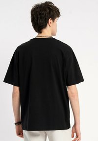 Czarna koszulka z krótkim rękawem z bawełny, o luźnym kroju, z okrągłym dekoltem i gładką fakturą, zaprezentowana od tyłu.