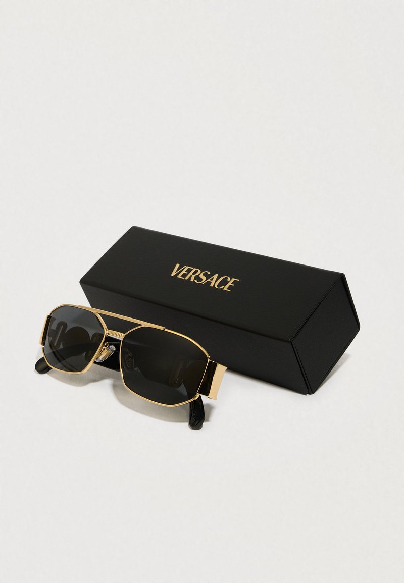 Occhiali da sole neri con accenti dorati in forma rettangolare, presentati in una scatola esagonale nera con l'etichetta "VERSACE". Stanghette nere lucide.