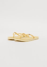 Tongs jaunes avec semelles plates et brides croisées. Semelle intérieure texturée avec un motif à pois. Conception légère adaptée aux vêtements décontractés.