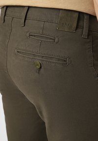 Olivgrüne Hose mit glatter Textur, ausgestattet mit zwei Gesäßtaschen, von denen eine mit einem Knopf versehen ist, sowie einem Lederlogo-Patch mit der Aufschrift "BRAX."