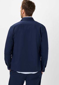 Chemise boutonnière bleu marine à manches longues, avec un col et une coupe droite. Texture douce avec une finition lisse, comportant des boutons aux poignets.