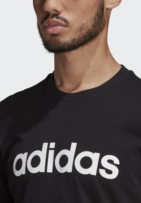 Mustat puuvillapaidat, joissa on pyöreä kaula-aukko. Ominaisuuksiin kuuluu näyttävä valkoinen "adidas" -logo rinnassa. Sileä rakenne ja rento istuvuus.