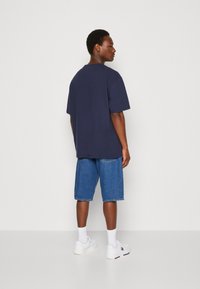 T-shirt in cotone blu navy con maniche corte, abbinato a pantaloni corti in denim azzurro chiaro. Sneakers bianche e calzini bianchi fino alla caviglia.